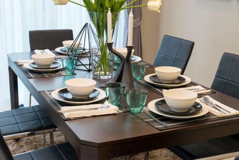 Dark wood dining room table with six place settings, comfortable modern  chairs and large central vase of flowers