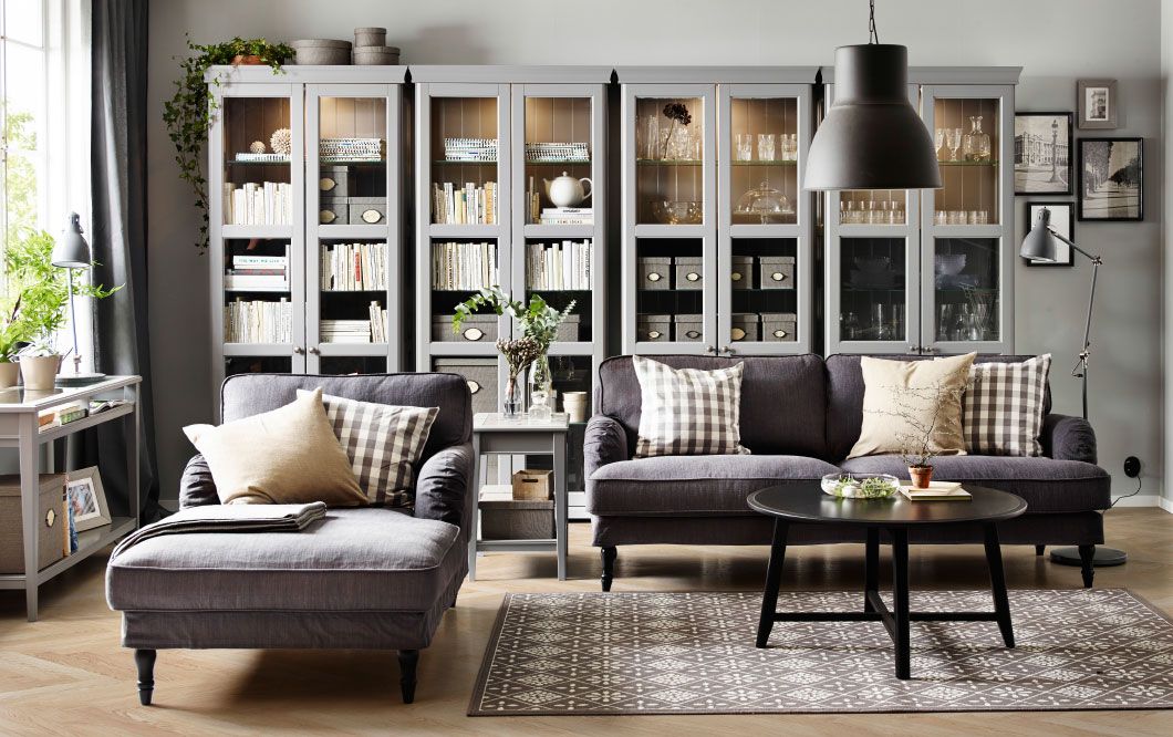 A living room with a grey three-seat sofa, chaise lounge and a black round  coffee table. Combined with four grey glass-door cabinets.