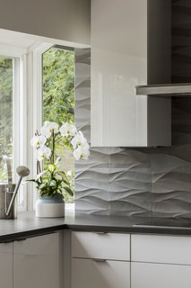 The undulating curves of the natural stone backsplash by Decorative  Materials Inc. work with the