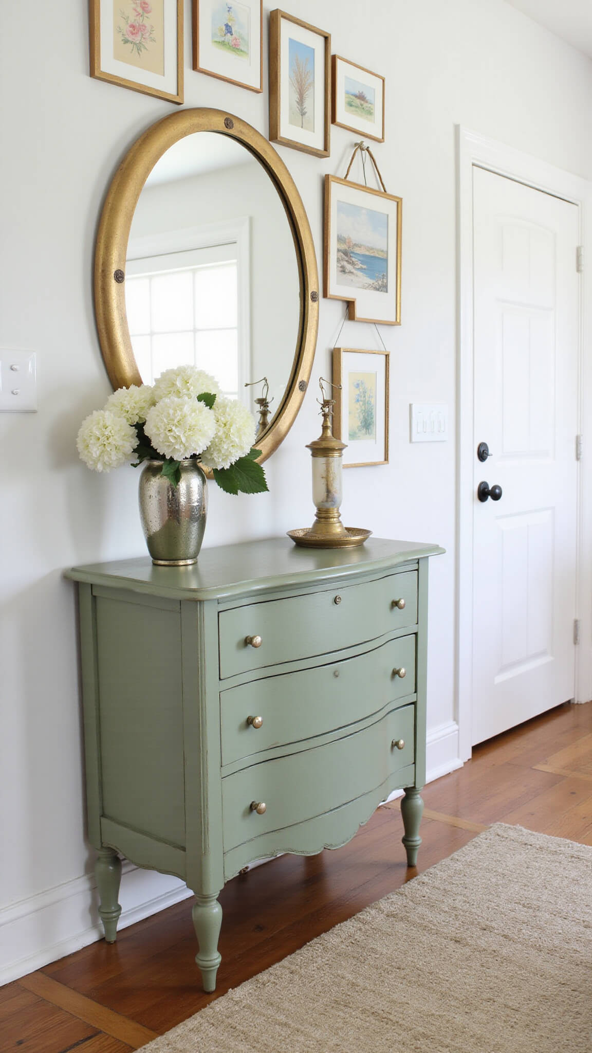 Charming vintage sage green dresser topped with a round gilt mirror, fresh white hydrangeas in a mercury glass vase, and a gallery wall featuring soft watercolor paintings.